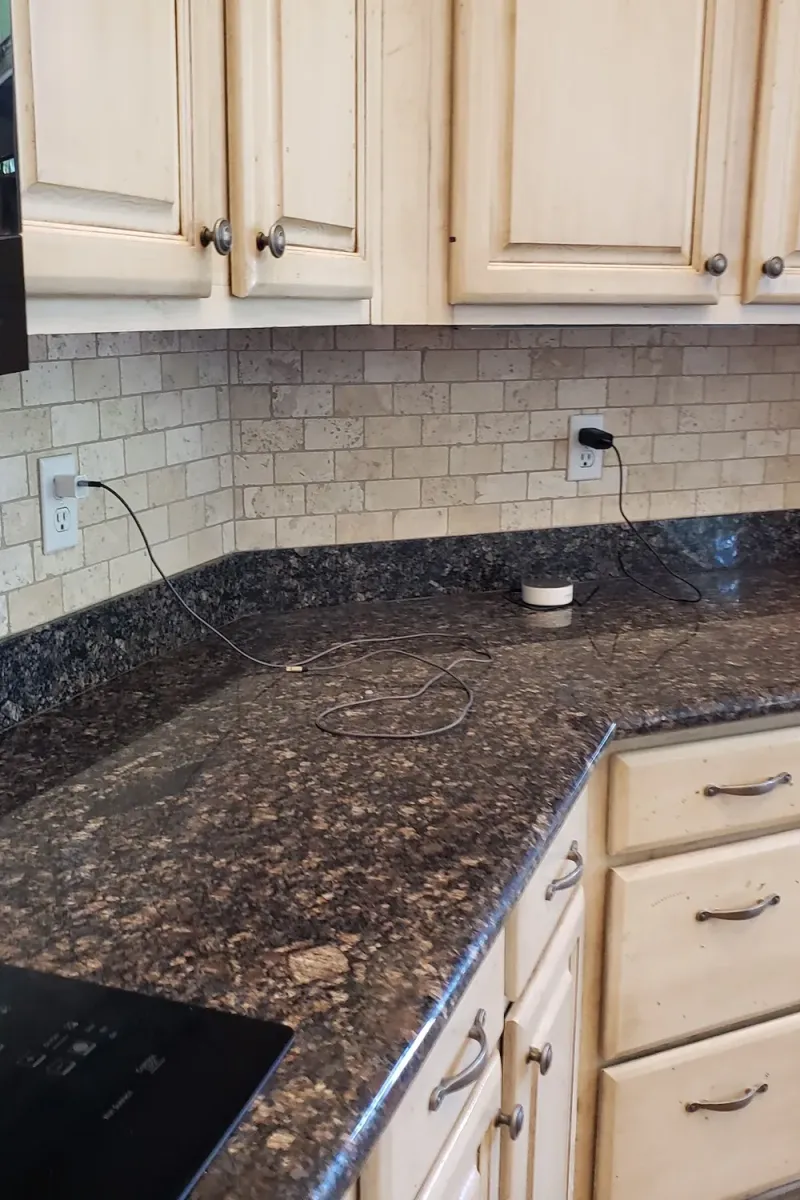 Cream kitchen cabinets around a granite corner counter, before painting