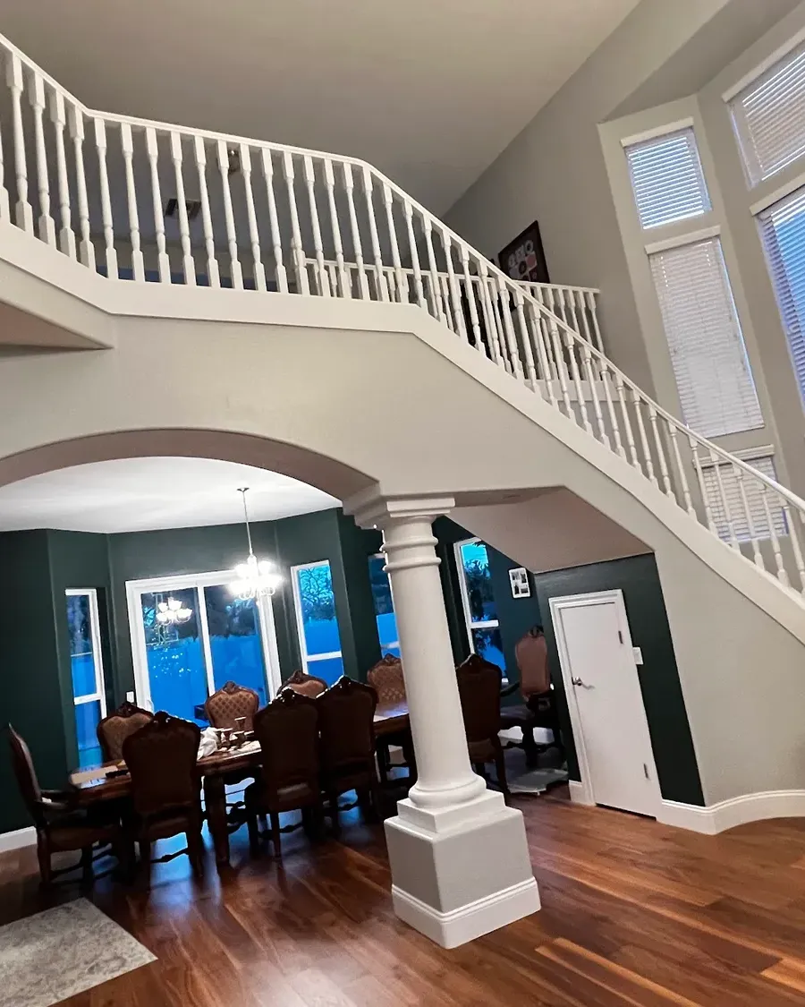 A freshly painted entry with a curved staircase, columns and a deep green dining room
