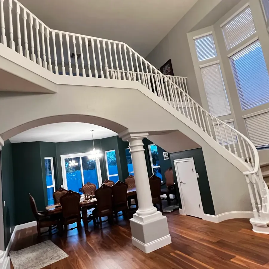 A freshly painted entry with a curved staircase, columns and a deep green dining room