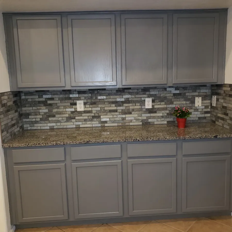 Grey painted kitchen cabinets under a stone mosaic backsplash