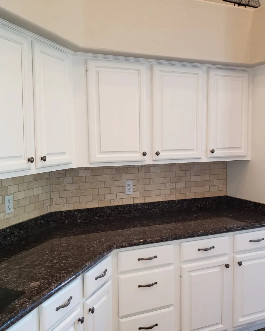 White painted kitchen cabinets around a dark granite corner counter
