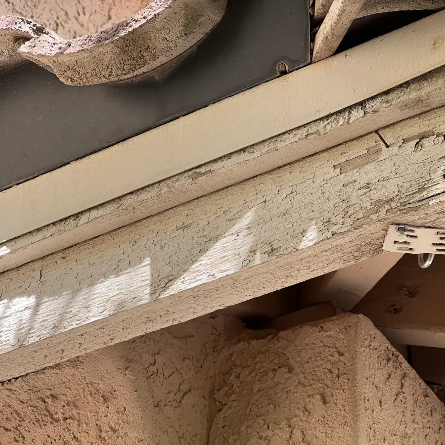 Paint peeling off a wooden fascia board under a tile roof