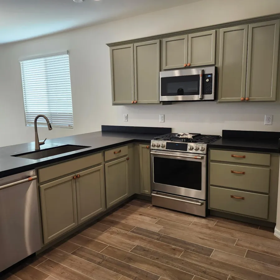 A kitchen with sage green painted cabinets and dark counters