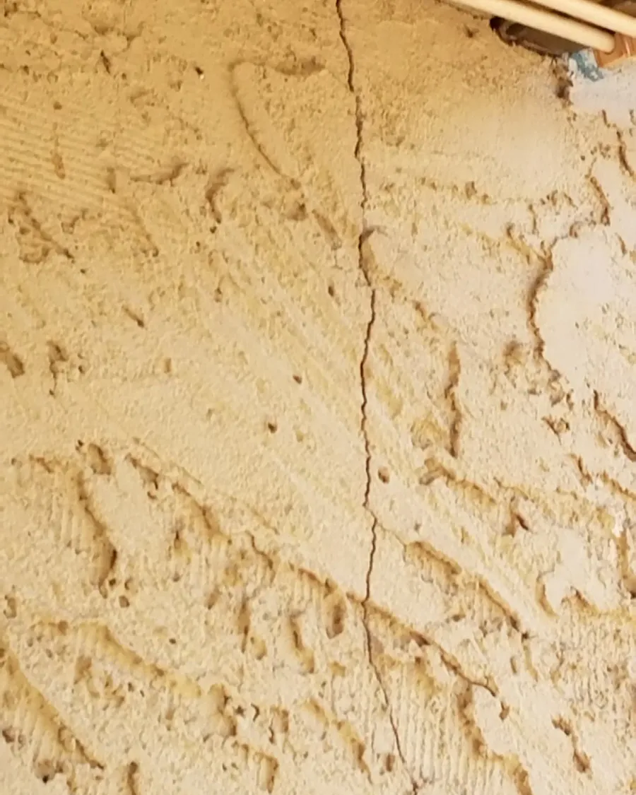 A long crack running down a textured stucco wall, before repair