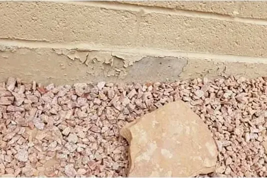 Stucco peeling along the base of an exterior wall above a gravel bed