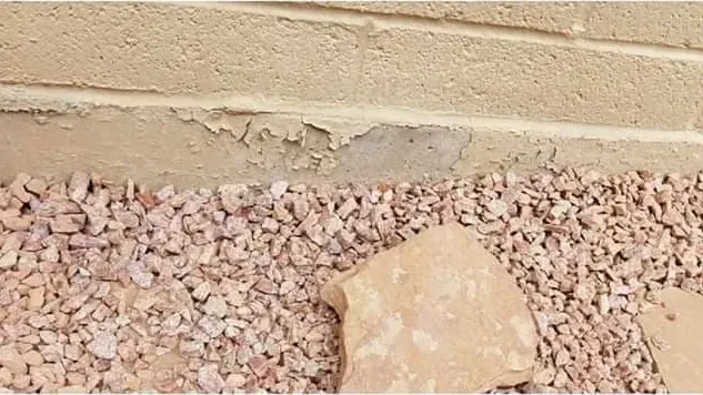 Stucco peeling along the base of an exterior wall above a gravel bed
