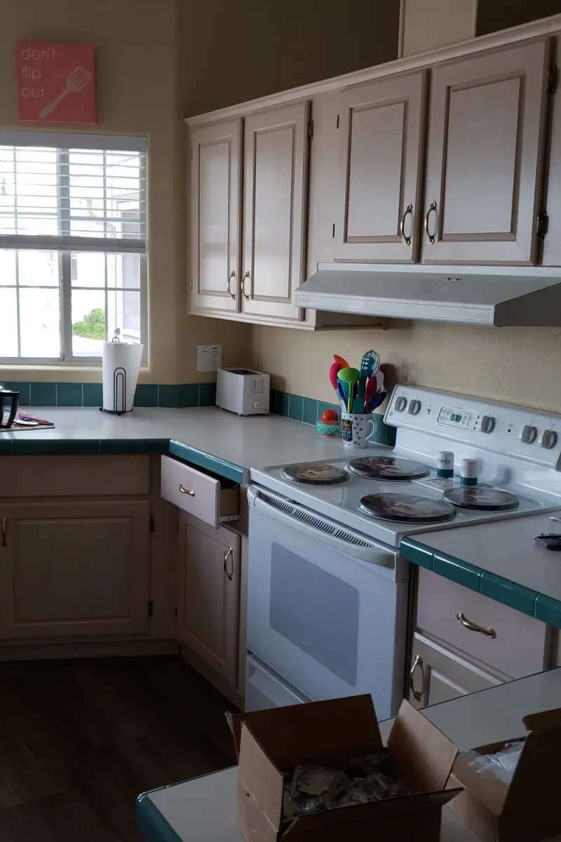 Tan kitchen cabinets beside a window, before painting