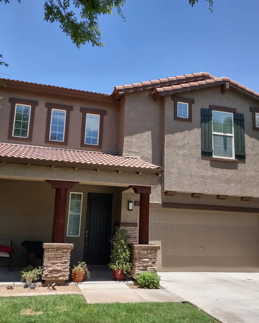 A two-story stucco home with a stone base and dark shutters, freshly painted