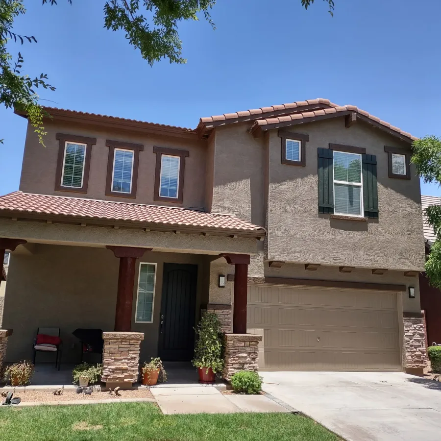 A two-story stucco home with a stone base and dark shutters, freshly painted