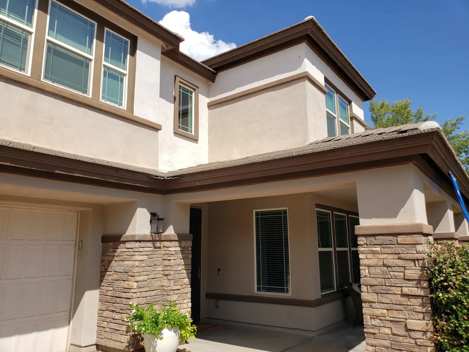 A two-story stucco home with stone columns, freshly painted