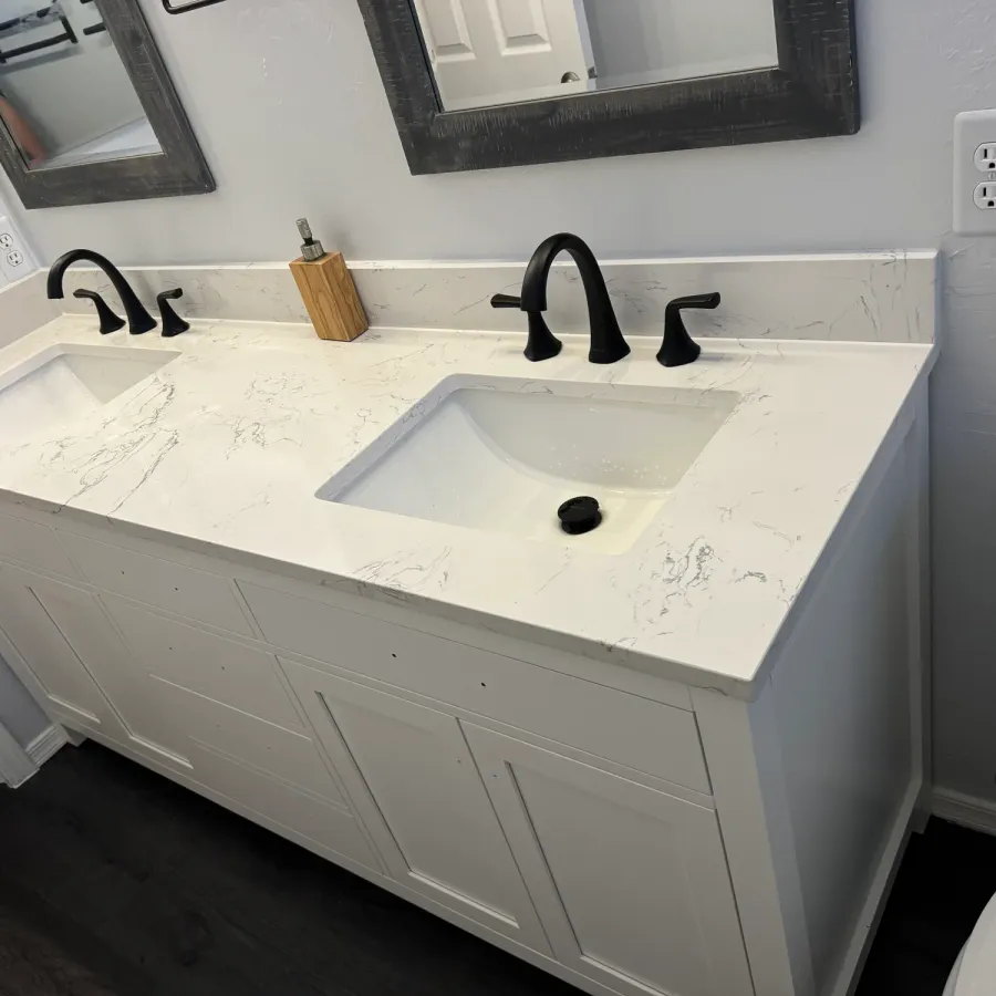 A white double vanity with black faucets and a marble-look top