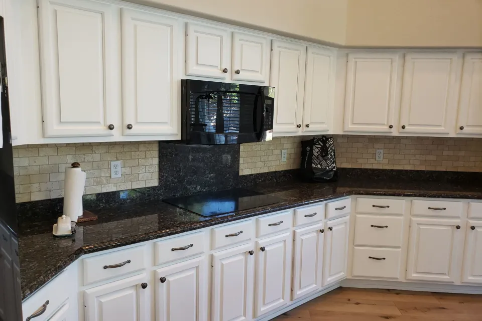A kitchen of white painted cabinets with dark granite counters and a tile backsplash