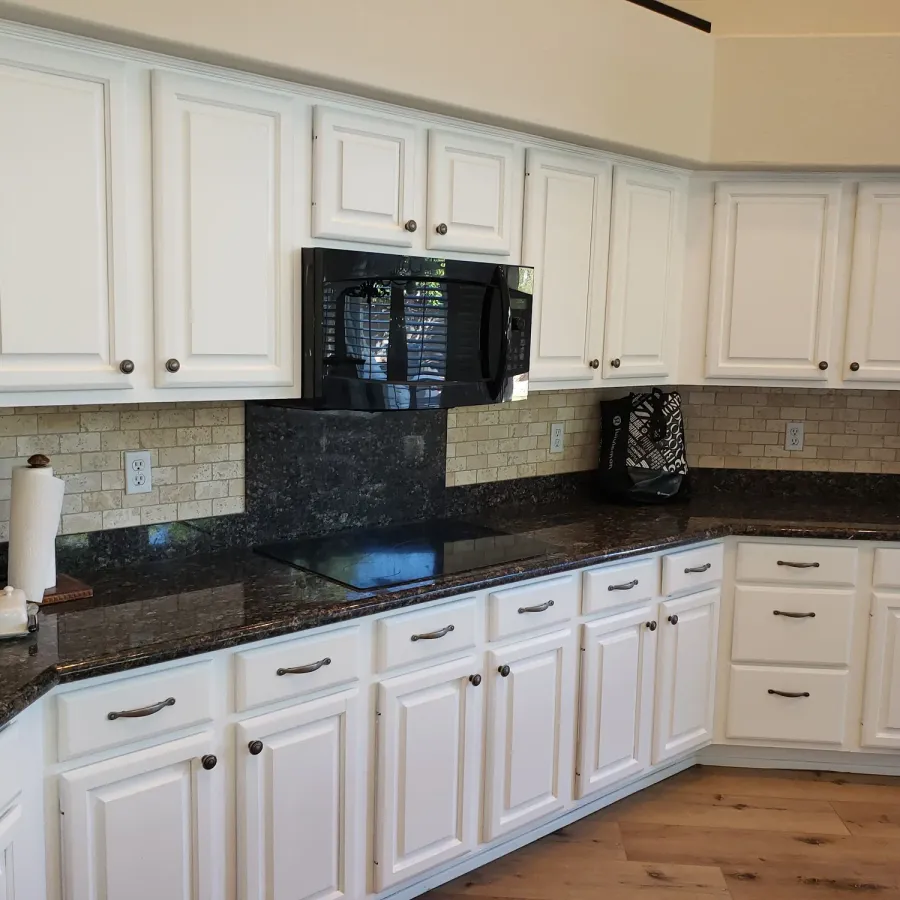 A kitchen of white painted cabinets with dark granite counters and a tile backsplash